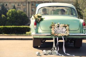 Hochzeitspaar im Auto mit Teller JUST MARRIED und Dosen im Freien dekoriert