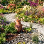 blumengarten mit ziersteinen und geschwungenem kiesweg rund um farbenfrohe beete